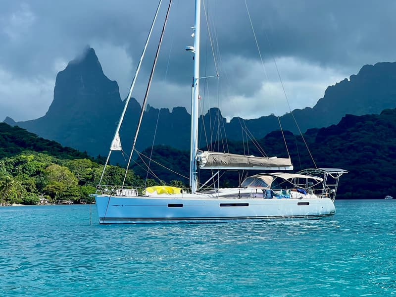Cyrolia, a white sailing yacht, at anchor in a turquoise lagoon beneath jagged green peaks.