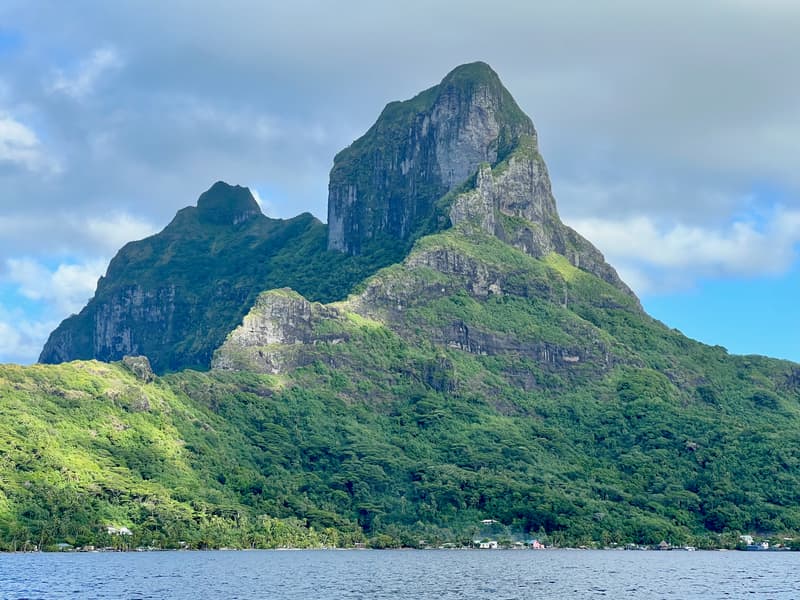 A steep, forested green peak rising above the lagoon, seen across the water.